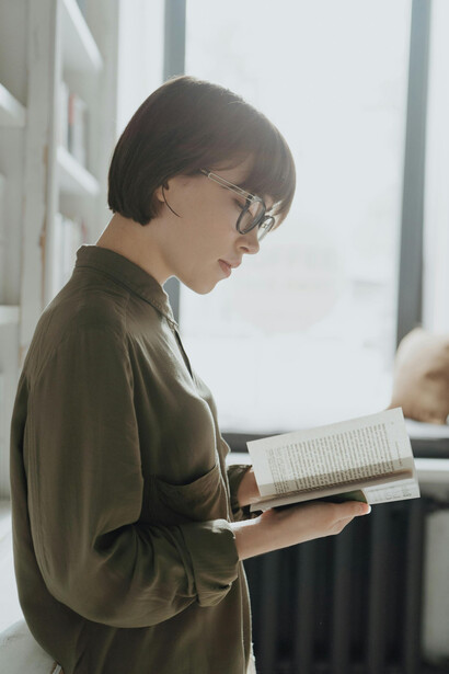 Una mujer leyendo un libro en una biblioteca iluminada por el sol