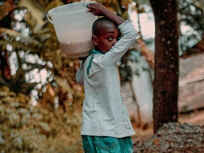 Young girl appears concerned as she carries goods to support her family