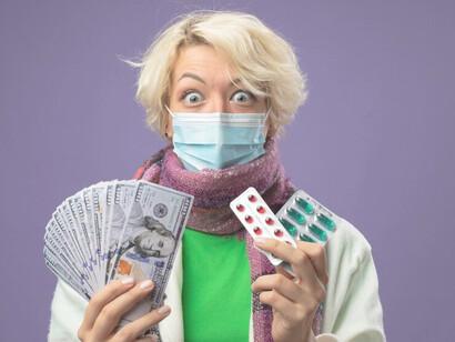 Unhealthy woman with short hair, wearing a warm scarf and facial protective mask, holding cash and a blister pack of pills while looking shocked at the camera, highlighting healthcare costs and economic challenges