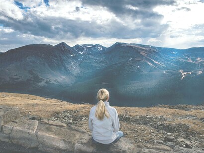 A woman sitting peacefully overlooking a mountainous region is soaking in the calm and reflecting upon the culture of peace