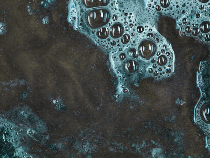 Foamy, chemical-laced water spreads across a dark surface, suggesting pollution beneath an abstract, almost organic pattern