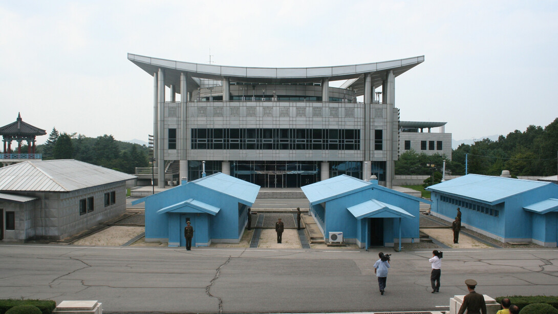 A view from South Korea toward North Korea in the Joint Security Area at Panmunjom, featuring military personnel from both North and South Korea, along with a U.S. soldier standing alongside them