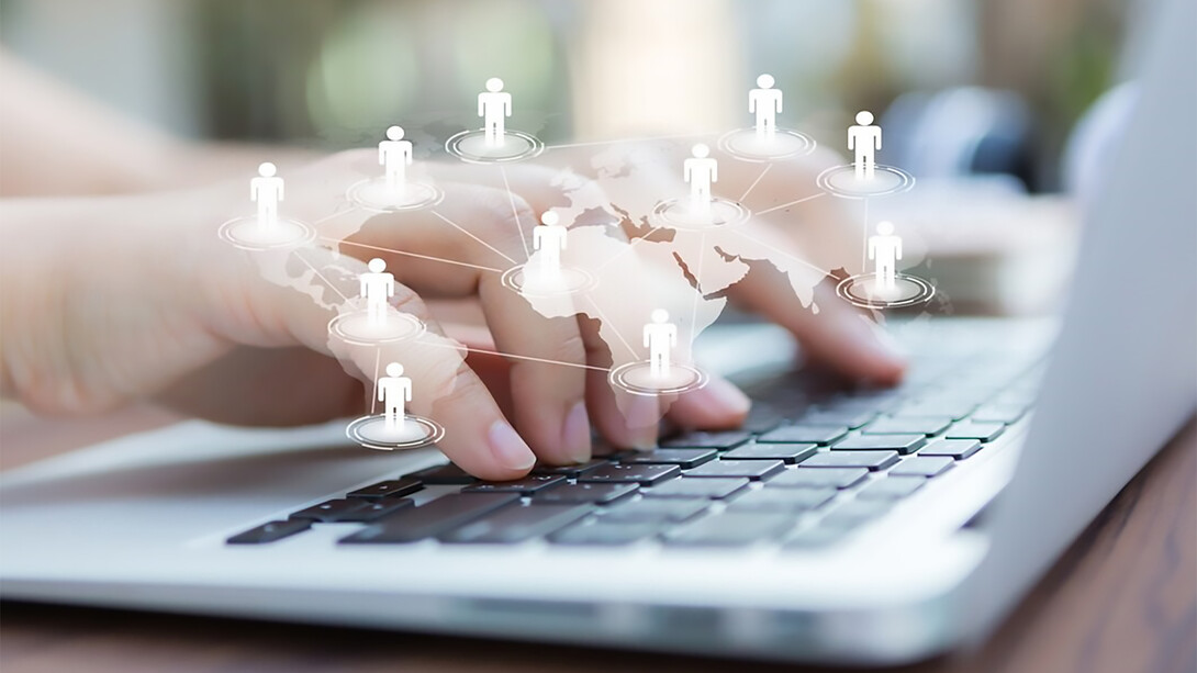 Hands typing on a laptop, with a virtual world map in the background, symbolize virtual interaction, social connection, and the power of digital communication