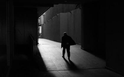 Una figura solitaria avanza por un pasaje oscuro hacia una zona iluminada, dejando una larga sombra sobre el suelo