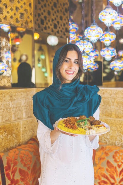 A woman showcasing a plate of Chelo Kebab, a quintessential dish in Iranian cuisine
