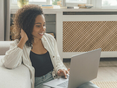 A woman wearing a white blazer works on a MacBook Pro at a brown wooden table