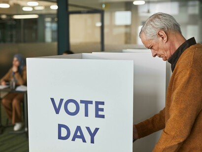 A man in a brown sweater stands by the polling station on voting day, surrounded by voters
