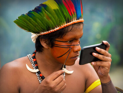 Indígena Tupi-Guarani usa um aparelho celular como espelho ao pintar o próprio rosto