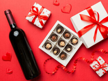 A bottle of red wine set against a vibrant background, paired with a gift box of heart-shaped chocolates
