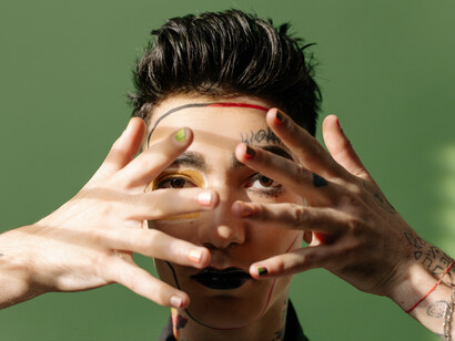 Mãos frente ao rosto evidenciam as cores pintadas nas unhas e o orgulho de usá=las