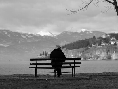 A senior man seated on a bench, facing the vast expanse of the sea