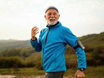 An elderly man running in nature, listening to music through earphones, enjoying a healthy lifestyle