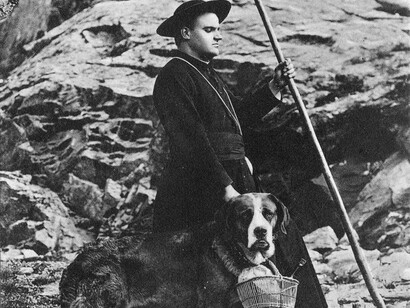 Cleric with dog carrying a basket, poses for the camera. Great St Bernard Hospice VS, around 1900–1910.
© Hospice du Grand-Saint-Bernard/Médiathèque Valais.