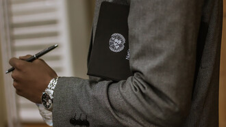 A man holding a black book with the UN emblem on it and a pen, symbolizing diplomatic and administrative work within the United Nations