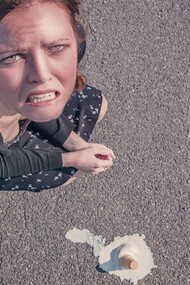 A woman, angry at herself, for dropping her ice-cream on the floor