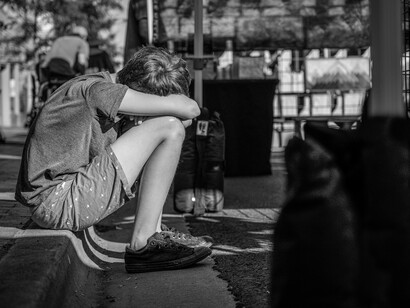 Boy sitting with his head on his knees on a curb