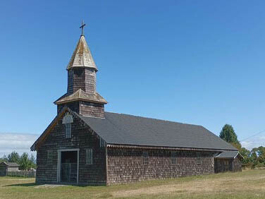 Las iglesias de la Escuela chilota de arquitectura religiosa en madera corresponden a templos católicos del sur de Chile que adscriben a la tipología artístico-arquitectónica que combina de manera original tanto la tradición centroeuropea de la torre-fachada como la latina de la planta basilical, y que se desarrolla principalmente en el archipiélago de Chiloé. Capilla Nuestra Señora del Tránsito, 2023,  Isla Meulin, Chiloé, Chile
