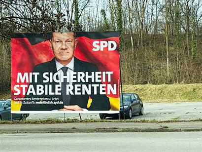 A rural roadside parking area with a billboard featuring German Chancellor Olaf Scholz
