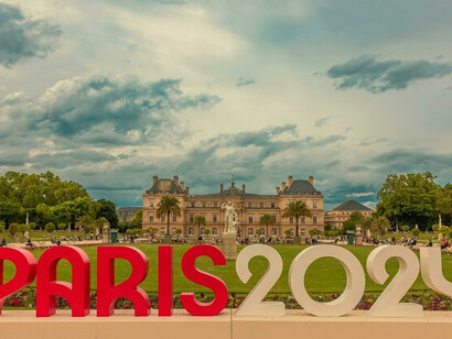 A promotional installation featuring a "Paris" logo in bold red letters; the Olympics promote themes of inclusivity, resilience, and sustainability