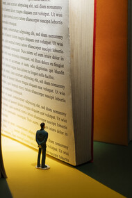 Small human figure reading it in the light hitting the huge book