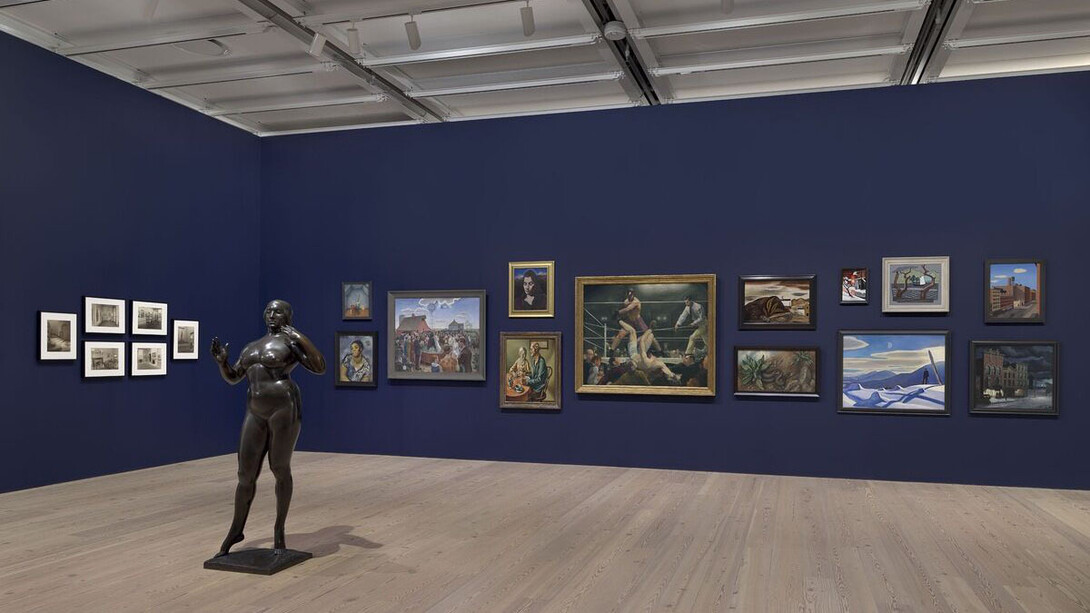 Installation view of The Whitney’s Collection: Selections from 1900 to 1965 (Whitney Museum of American Art, New York, June 28, 2019- ). Left wall: Six photographs by Charles Sheeler, (No title), 1933. Center of room: Gaston Lachaise, Standing Woman, 1912-27. Right wall, left to right, top to bottom: Madeline Shiff, Wiltz at Work, 1932; Anne Goldthwaite, Rebecca, c. 1925; John Steuart Curry, Baptism in Kansas, 1928; John D. Graham, Head of a Woman, 1926; Thomas Hart Benton, The Lord is my Shepherd, 1926; George Bellows, Dempsey and Firpo, 1924; Yasuo Kuniyoshi, Landscape, 1924; Katherine Schmidt, The Snake, 1932; Oscar Bluemner, Last Evening of the Year, c. 1929; Stuart Davis, Early American Landscape, 1925; Rockwell Kent, The Trapper, 1921; George C. Ault, Hudson Street, 1932; Charles Burchfield, Winter Twilight, 1930. Photograph by Ron Amstutz