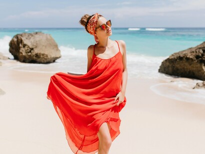 A woman in a beach-appropriate outfit, with the vibrant red color of the garment and the presence of accessories suggesting a personal style that balances practicality and visual interest