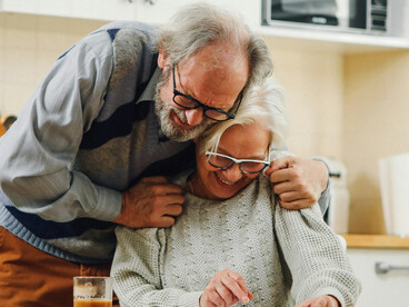 An elderly couple reading a document in their kitchen, laughing together in a moment that reflects the strength of a long-term relationship