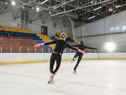 A girl dressed in a pink and black bodysuit skates gracefully in a cold, quiet arena, highlighted by a single spotlight