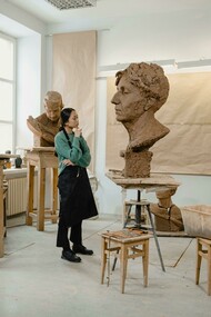 A sculptor works in his art studio, surrounded by tools and unfinished pieces