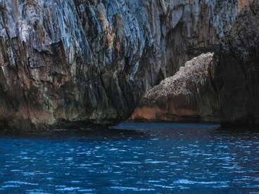 Towering volcanic cliffs enclosing a dark blue sea cave, symbolizing the wild coastline and hidden adventures that is found in Milos
