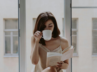 Bathed in soft morning light, a woman reads by the window, her thoughtful expression suggesting a moment of gentle melancholy