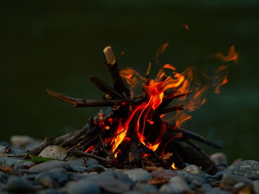 A small campfire glowing by a river, representing the warmth of shared wisdom passed from one generation to the next
