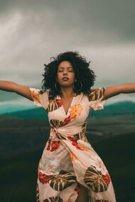 A woman in a white and red floral dress standing on a green grass field, representing freedom, self-acceptance, and openness