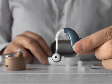 A close-up of a doctor showcasing a hearing aid, reflecting the intersection of medicine, technology, and human augmentation