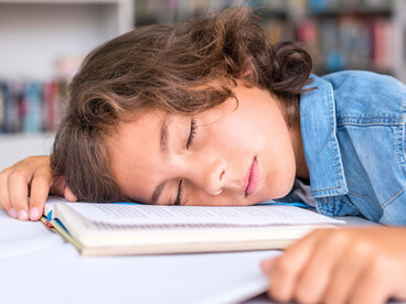 A child napping, overwhelmed by academic material, reflecting the cognitive strain linked to shortened attention spans