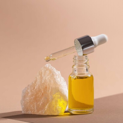 A bottle of argan oil with a dropper rests on a light-colored stone, perfect for moisturizing coily, and texturized hair