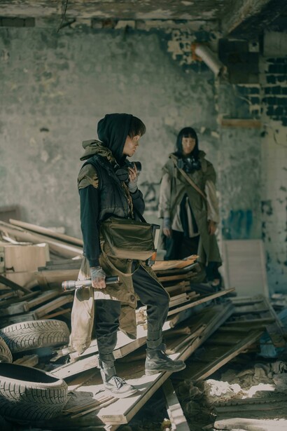Inside the shattered remains of a ruined structure, a man and a woman share a moment of fragile intimacy