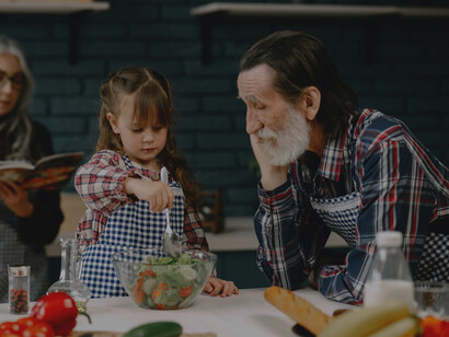 Granddaughter helping stir the salad in the kitchen with Grandpa