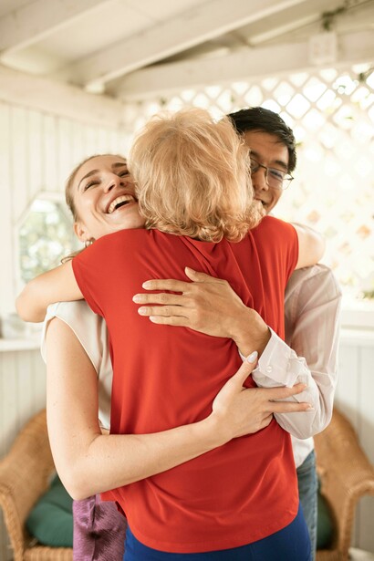 Back view of an elderly woman hugging a couple