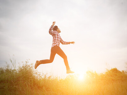 Un uomo con una camicia a quadri salta in aria, con lo sfondo del cielo luminoso e dell'erba, in un'atmosfera di libertà e gioia