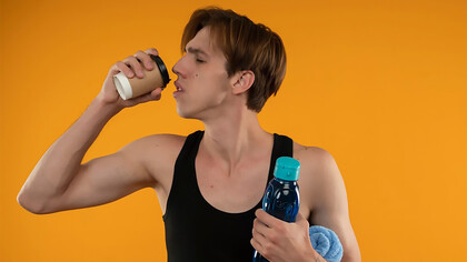 A young, sporty guy holding a towel and a water bottle, while drinking both coffee and an energy drink, highlighting a combination of hydration and energy consumption