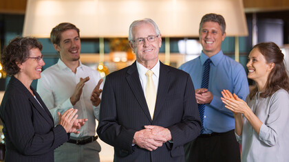An experienced leader standing confidently before colleagues, proud and smiling