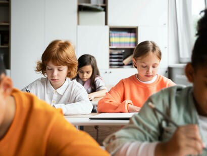 In un'aula, diversi bambini sono seduti a dei banchi e lavorano concentrati sui loro quaderni