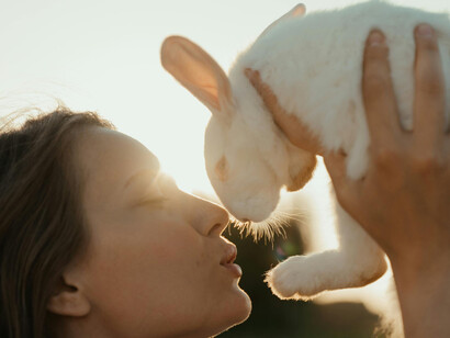 A blond girl holding a white rabbit to her face, touching noses
