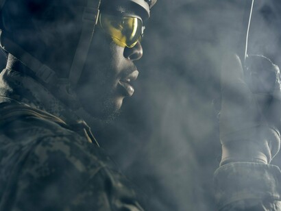 A soldier standing in dense smoke with weapon in hand, representing the violence that continues to destabilize communities