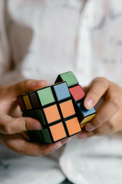 A close-up of a person's hands holding and manipulating a Rubik's Cub, a challenging mental task that requires focused attention, strategic thinking, and the ability to adapt to setbacks