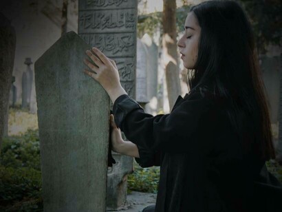 A woman feeling the tombstone of the buried at a cemetery 