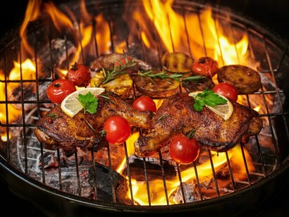 Grilled chicken legs on the flaming grill with grilled vegetables with tomatoes, potatoes, pepper seeds, salt