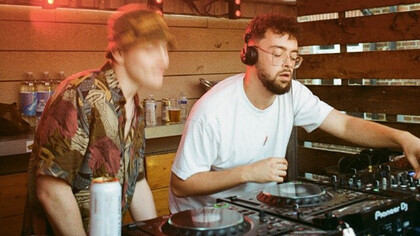 A bespectacled DJ spins mesmerizing beats, while the man beside him dances with unbridledly
