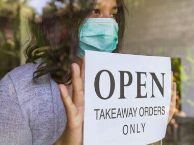 A small business owner impacted by COVID-19 holds a sign reading, "Open for takeaway orders only"